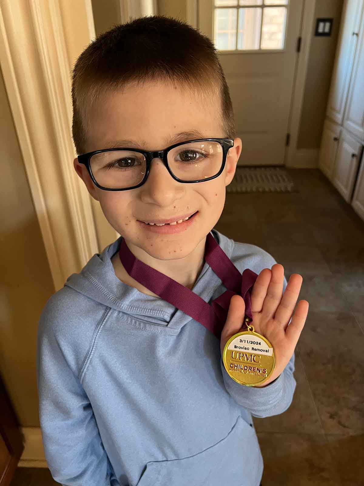Boy in a blue sweatshirt holding a medal.