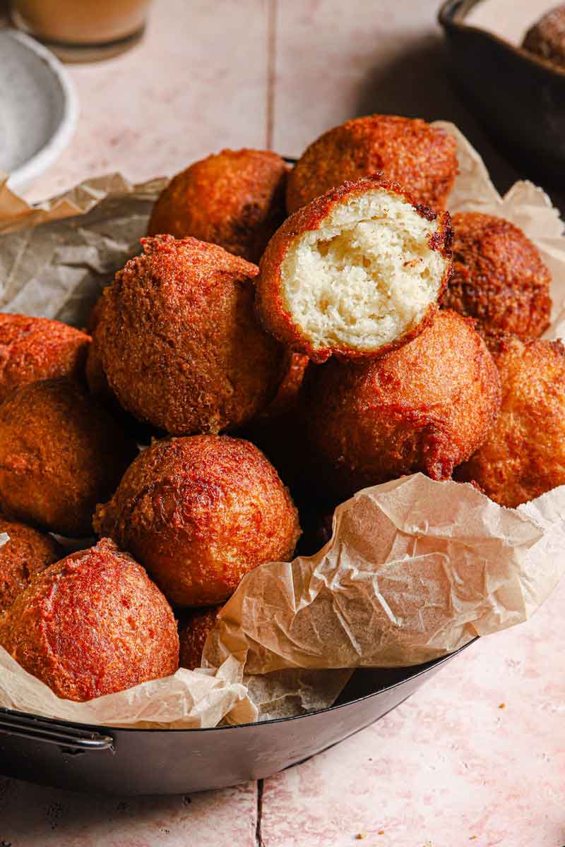 A pile of fried zeppole on parchment-lined bowl with a bite taken out of the one on top.