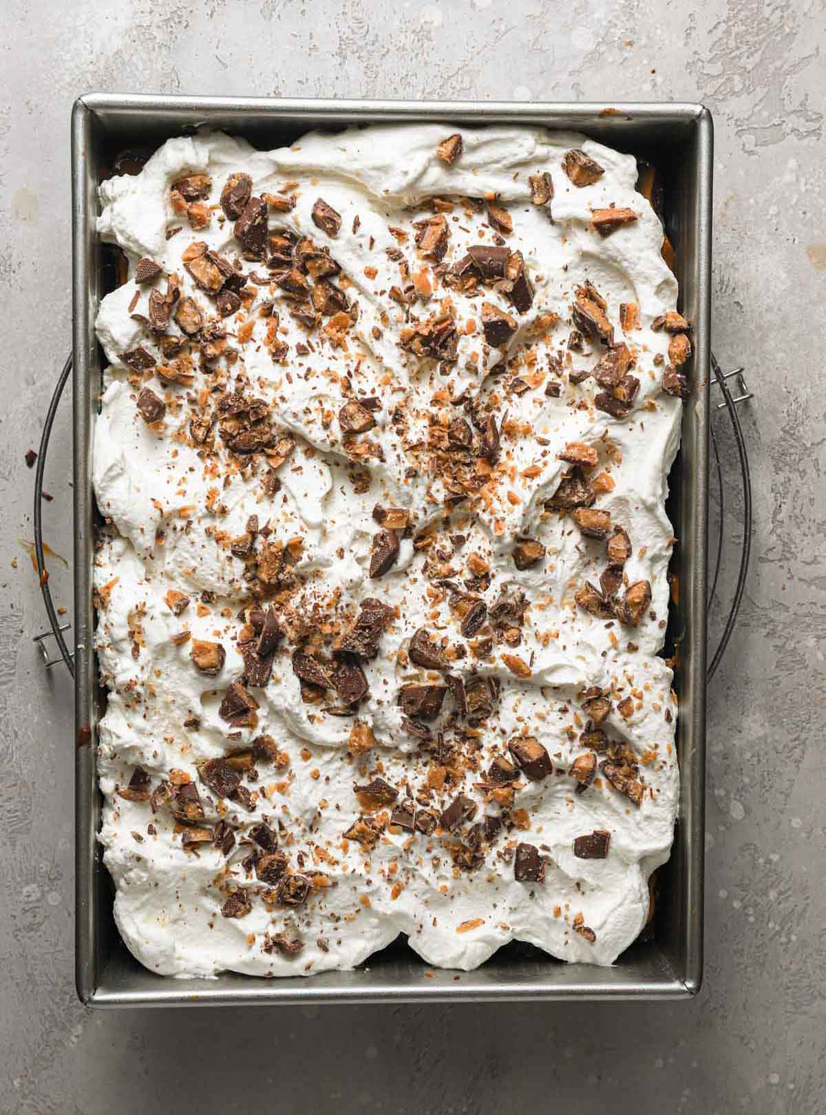 Overhead photo of assembled better than sex cake topped with whipped cream and crushed Heath bars.