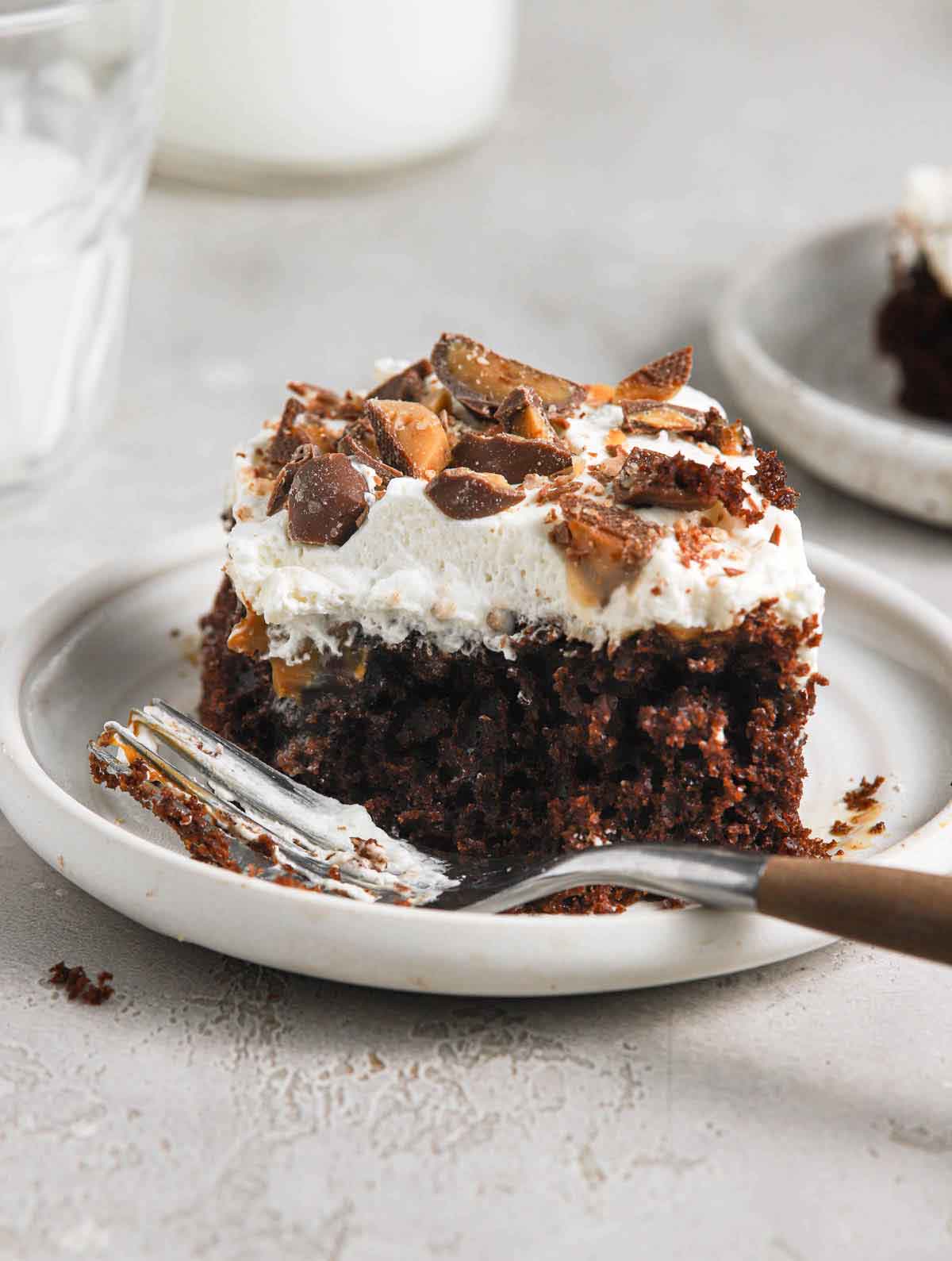 A single slice of better than sex cake on a rimmed white plate with a fork.