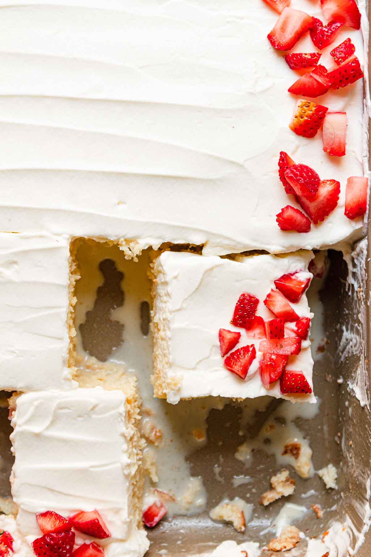 Close up overhead photo of tres leches cake in pan with two pieces cut away from the rest of the cake.