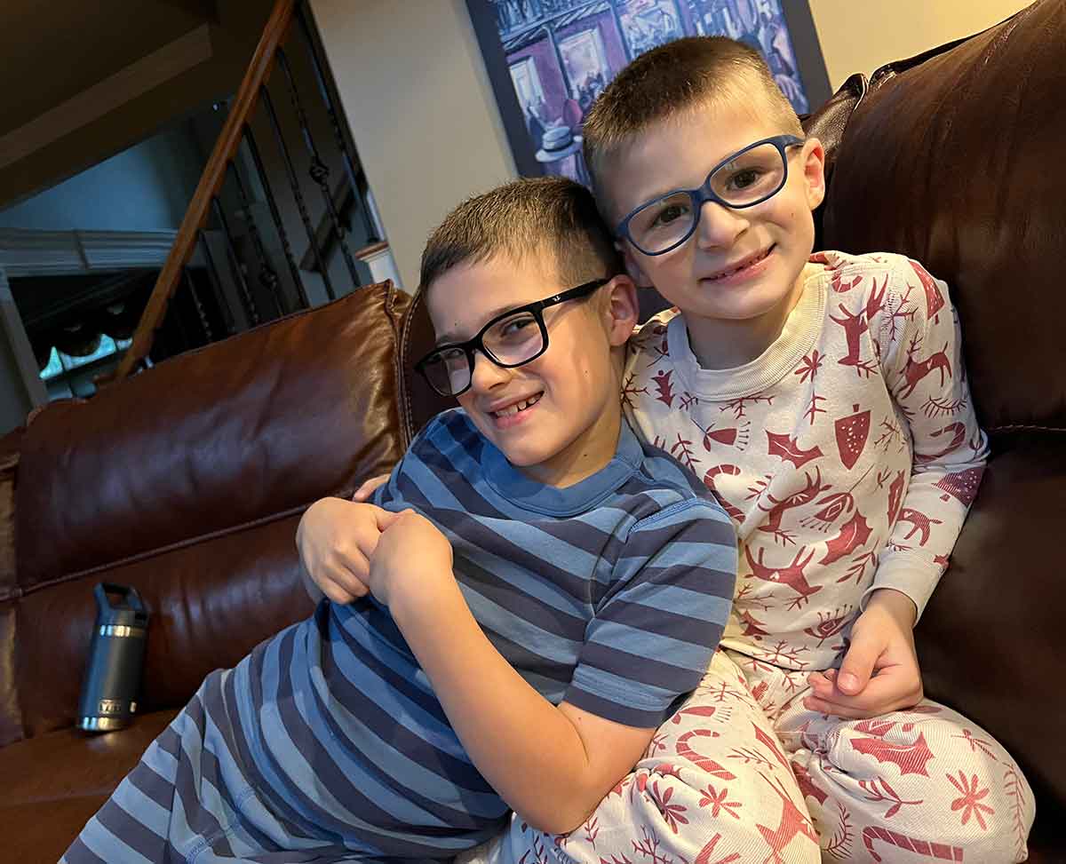 Two boys in pajamas hugging on a couch.
