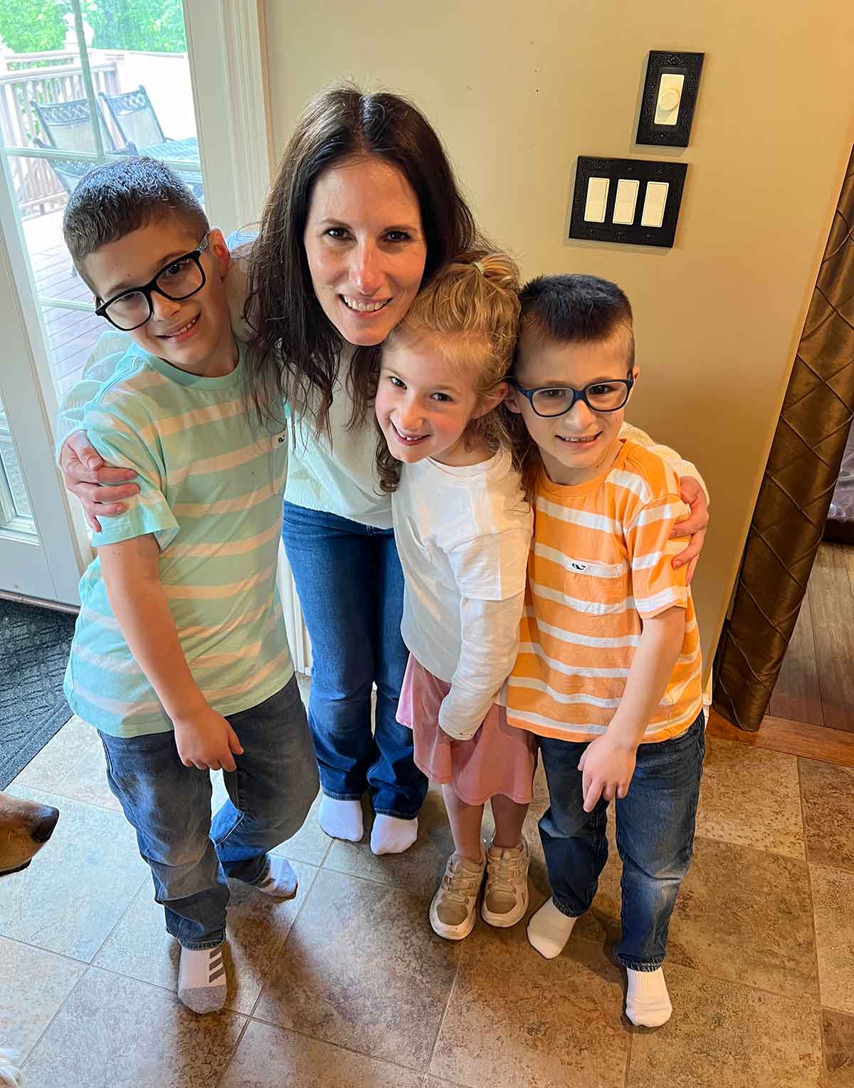 Woman hugging three kids, two boys and one girl.