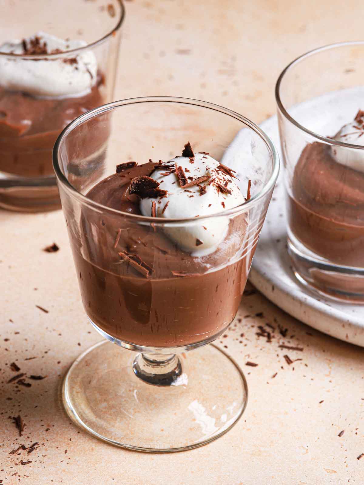 Small glass cups filled chocolate pudding and topped with whipped cream and chocolate shavings.