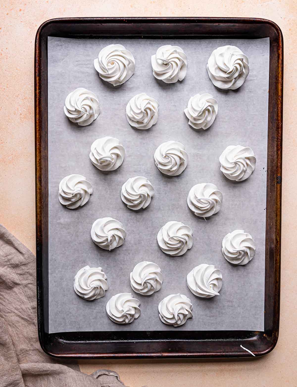 Overhead photo of meringue piped onto a parchment-lined baking sheet.