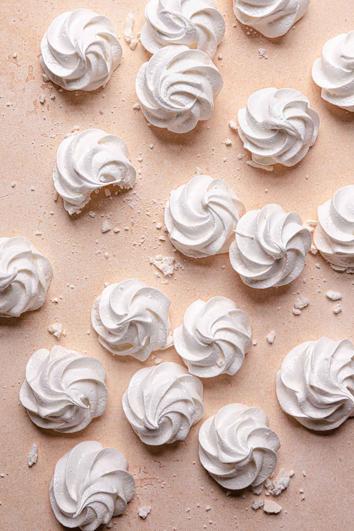 Overhead photo of meringue cookies spread out on a pink background.