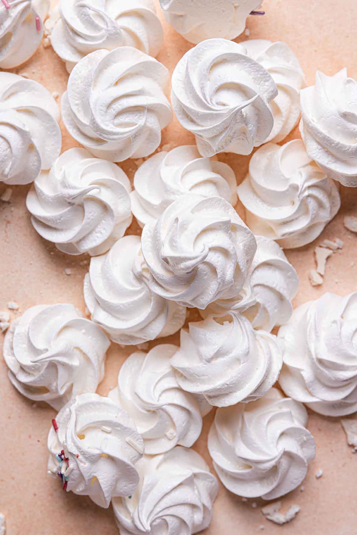 Overhead photo of meringue cookies on a pink background.