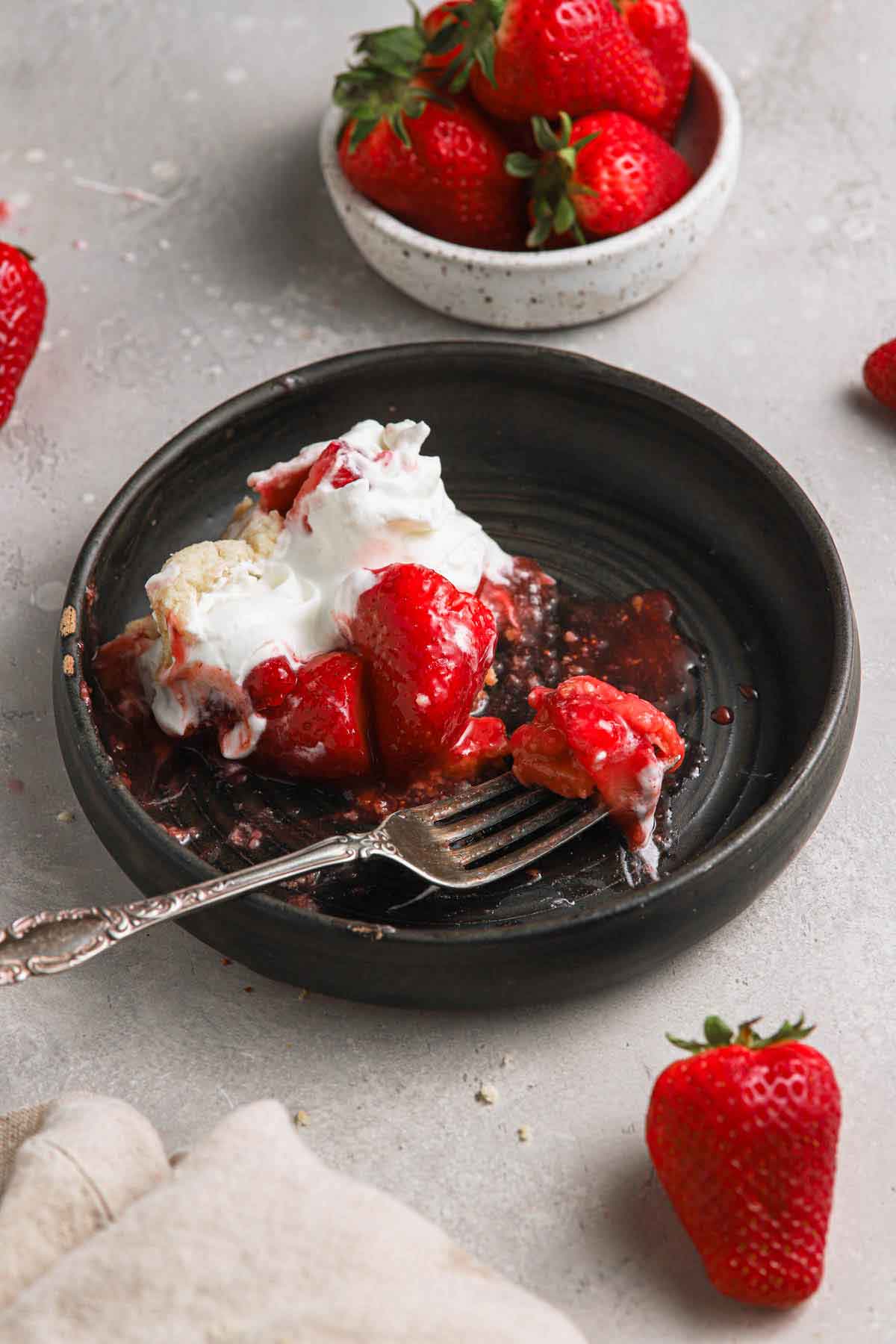 Slice of strawberry pie half-eaten on a black plate with a fork on it.