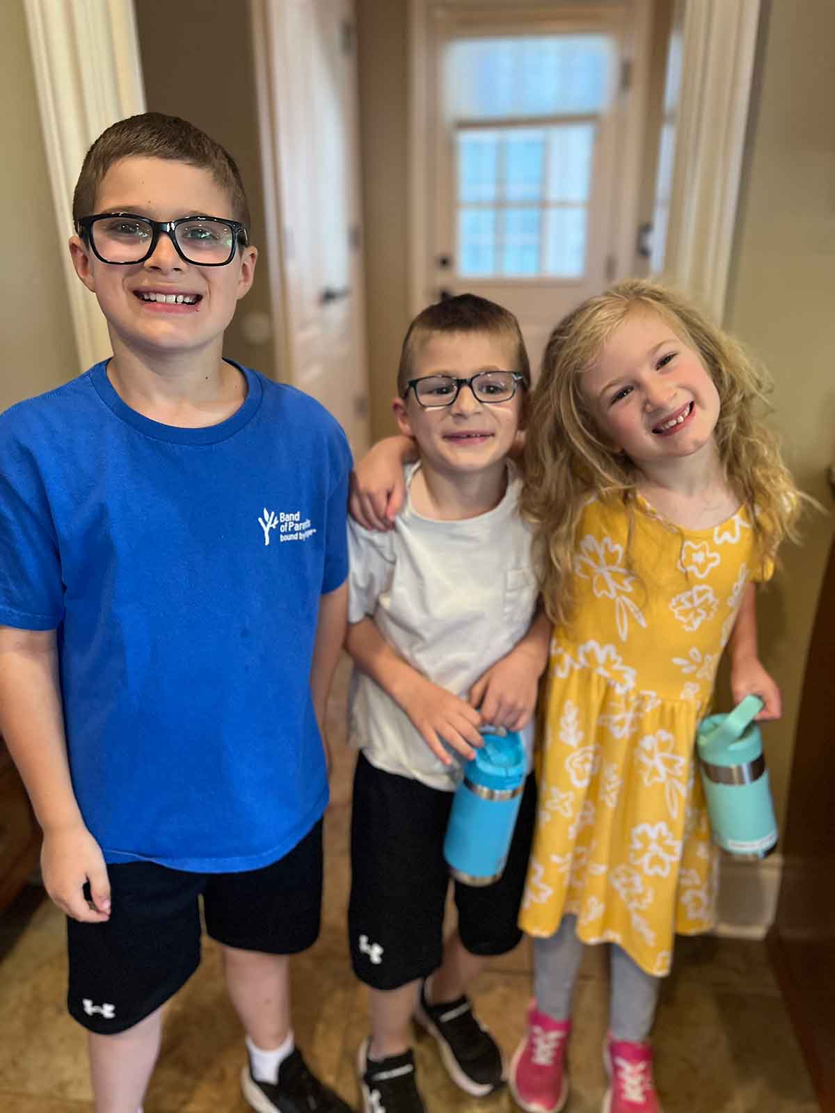 Two boys and a girl with their arms around each other, smiling.