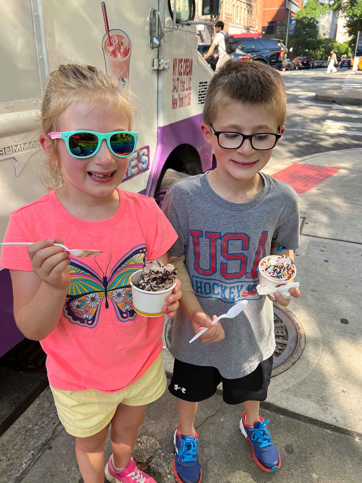 Little girl and boy eating cups of ice cream on a sidewalk in New York.