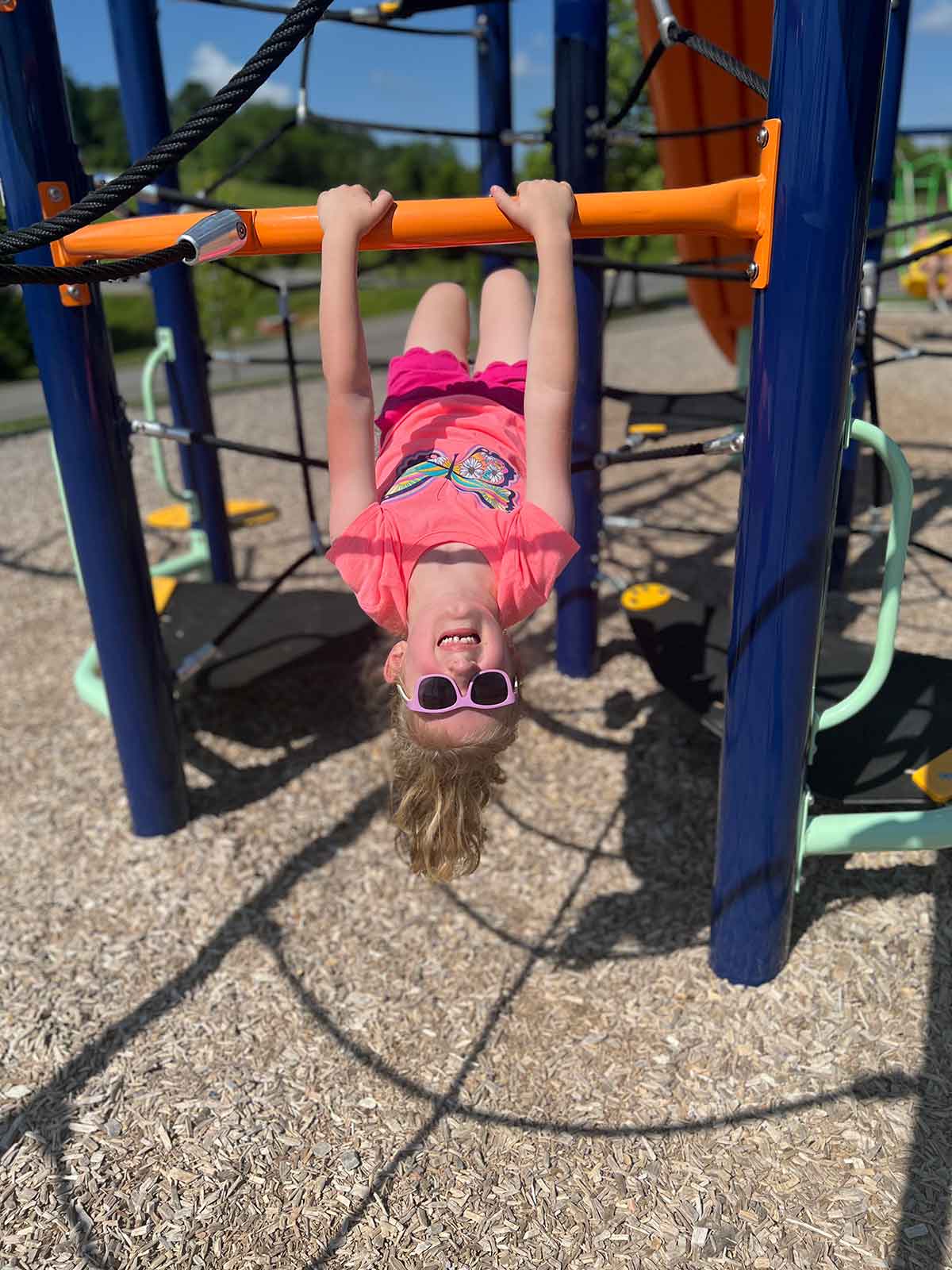 Little girl hanging upside down on playground equipment.