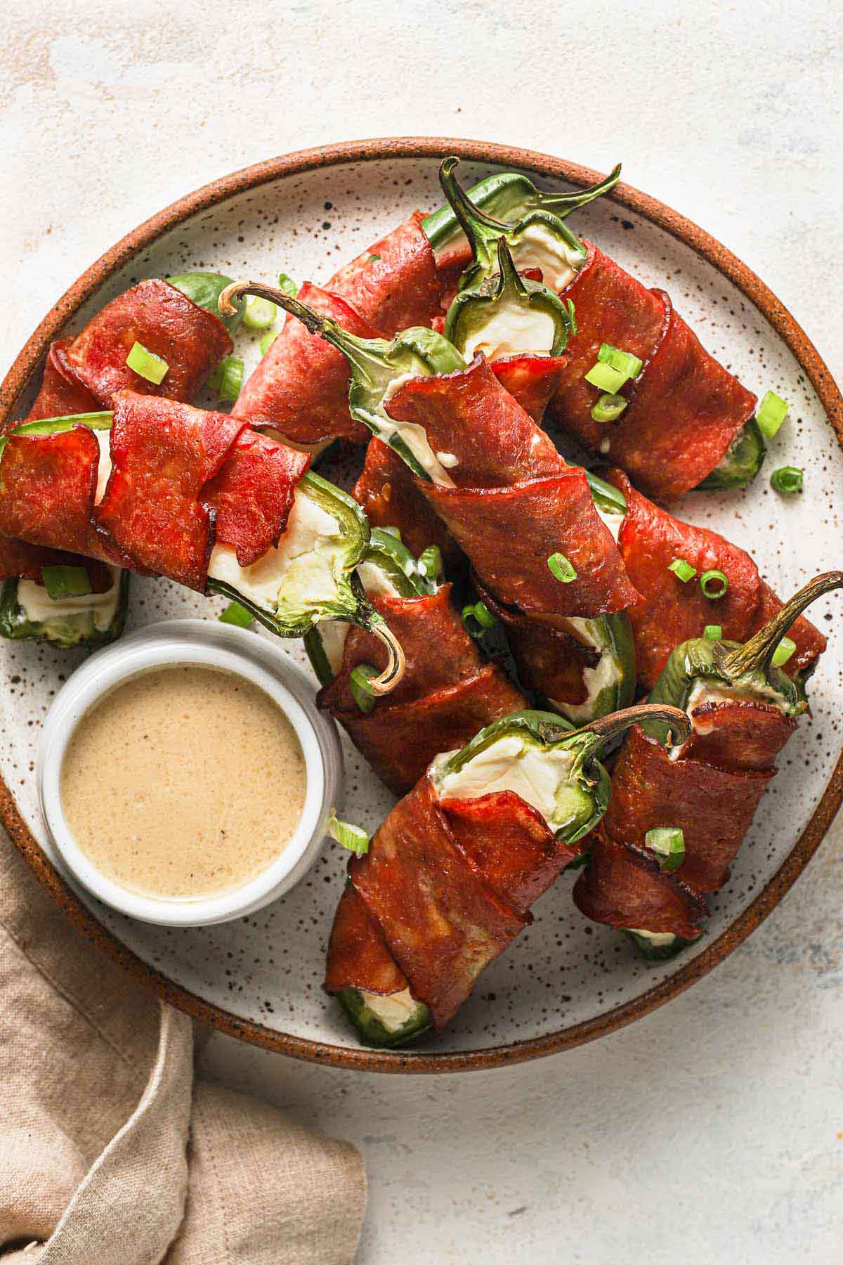 Jalapeno poppers arranged on a plate with a cup of dipping sauce on the side.