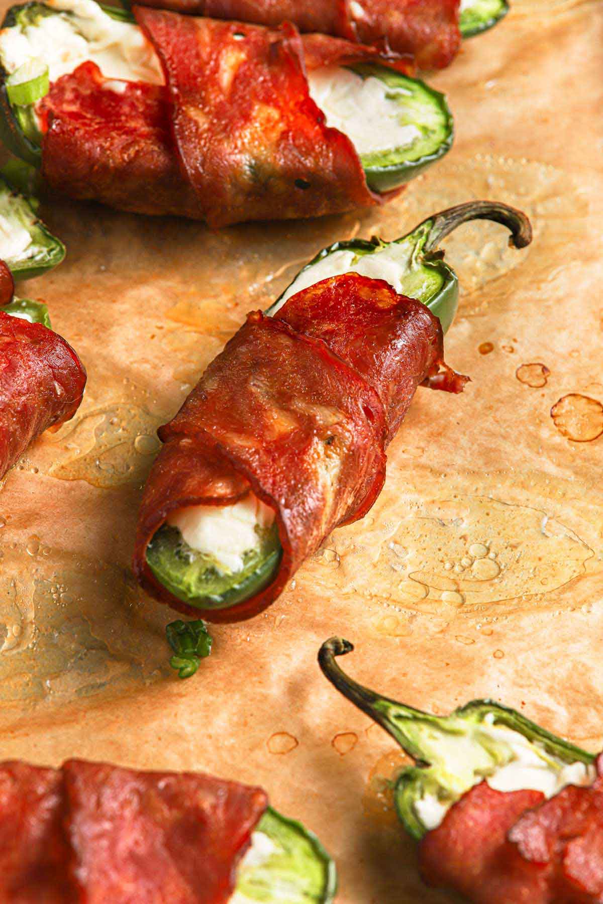 Close up photo of baked jalapeno poppers on brown parchment sheet.