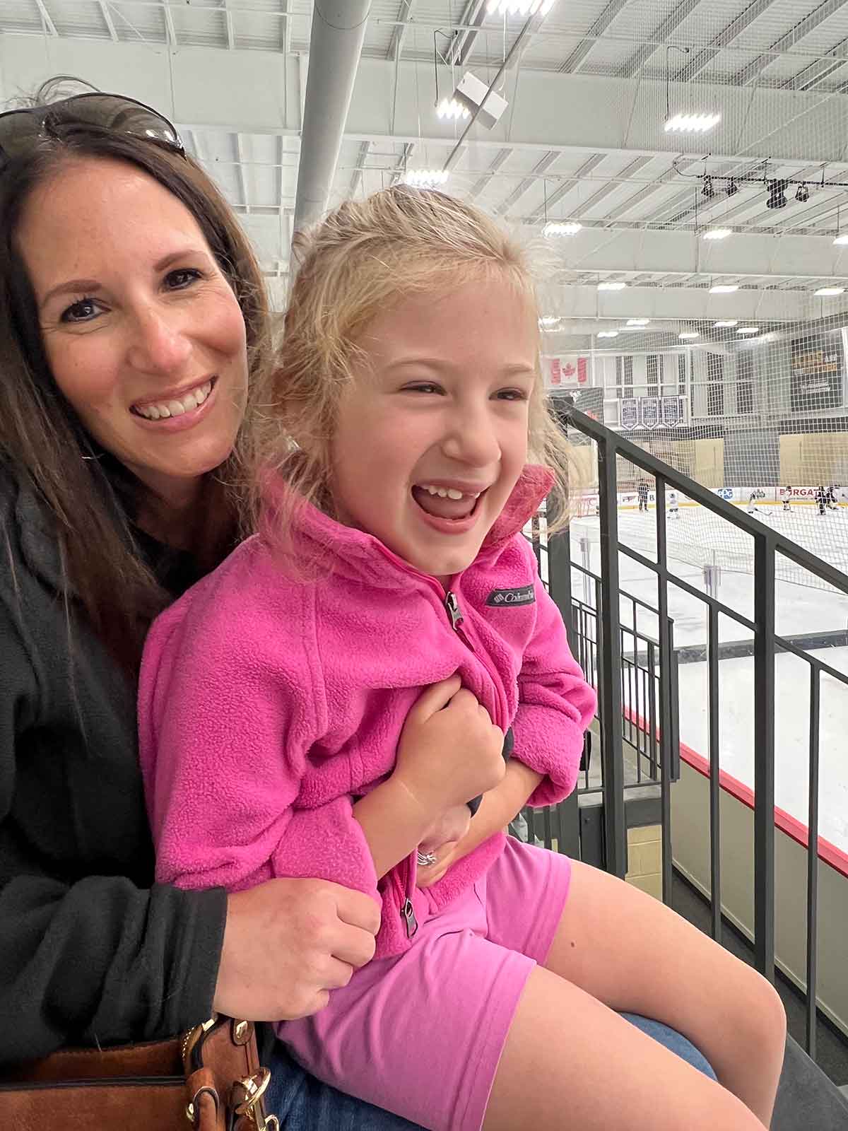 Mom with daughter sitting on her lap at an ice rink.