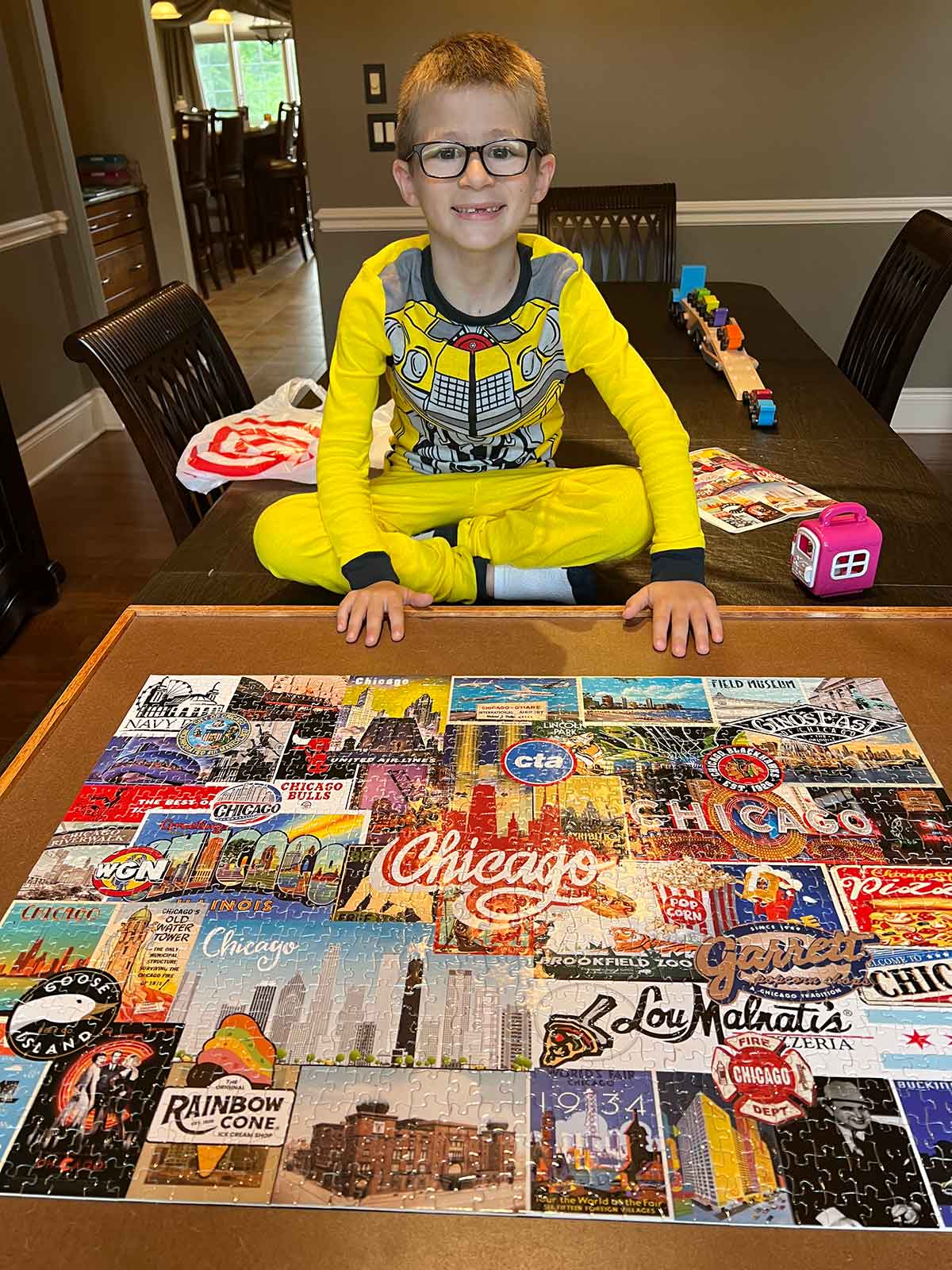 Little boy sitting on top of a table in front of a completed puzzle.