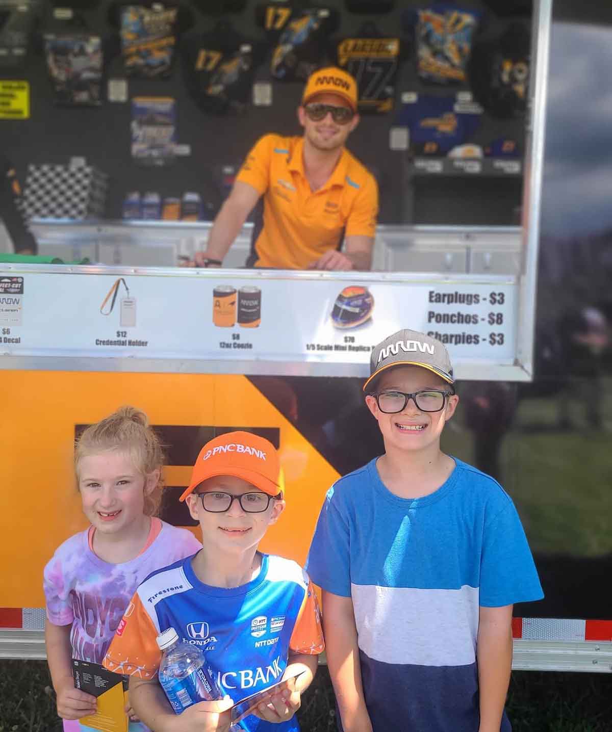 A girl and two boys standing in front f a race car driver at an autograph session.