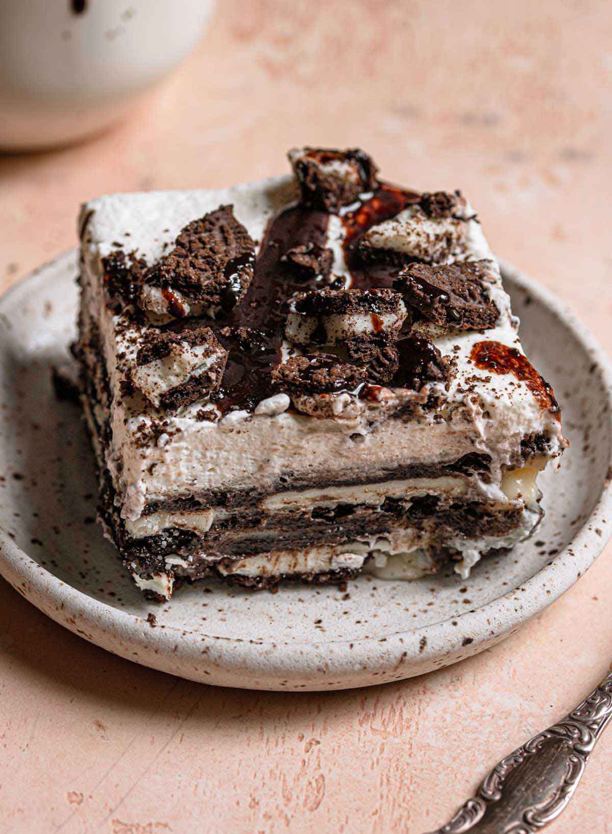 A square slice of Oreo icebox cake on a white speckled plate.