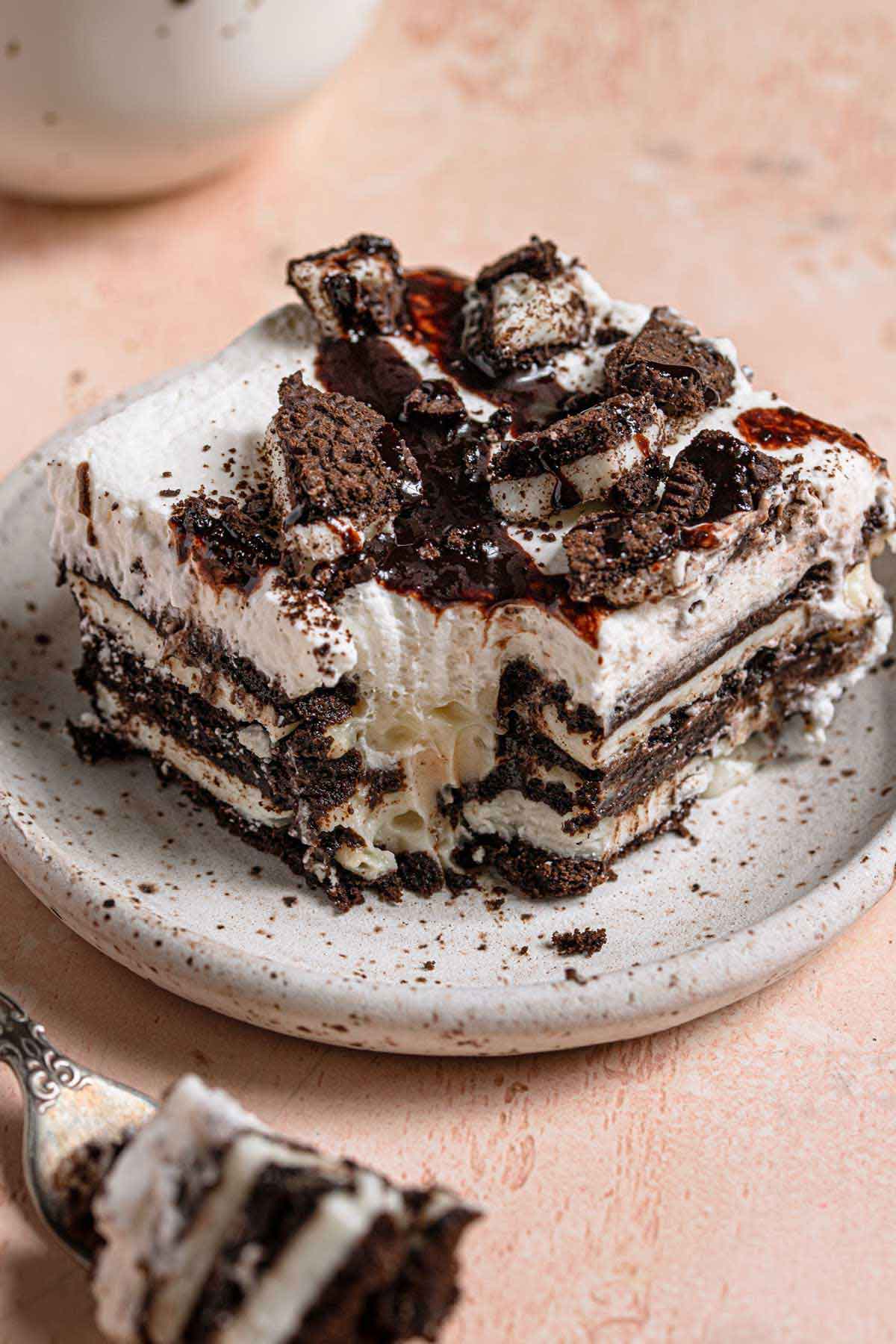 Square slice of Oreo icebox cake on a white speckled plate with a forkful taken out of the corner.