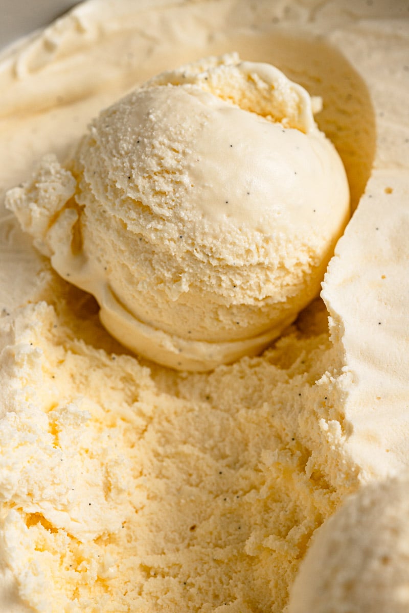 Single scoop of vanilla ice cream scooped and still sitting in container of homemade ice cream.