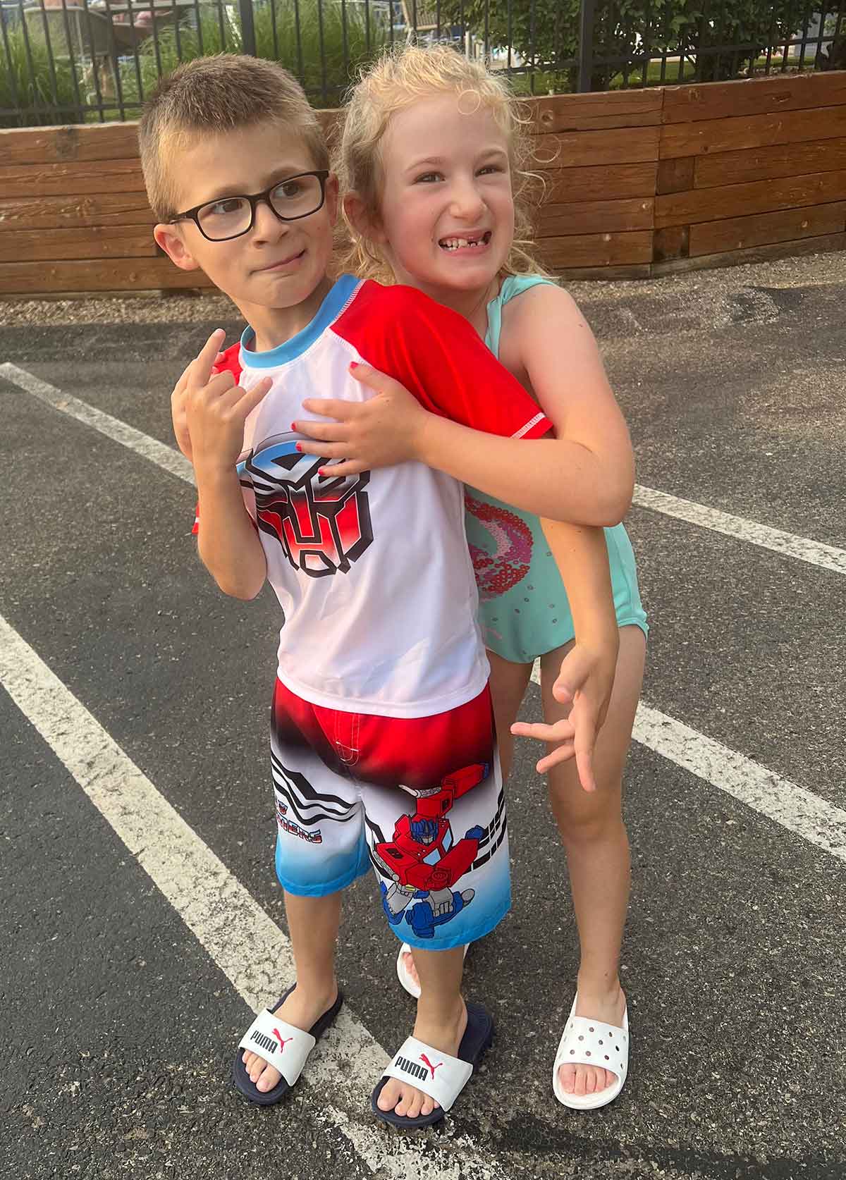Girl hugging a boy from behind, both in swimsuits.