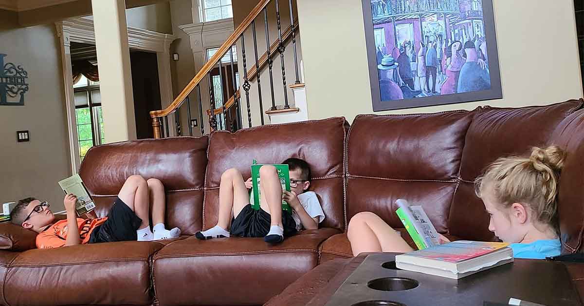 Three kids sitting spread out on a couch, all reading books.