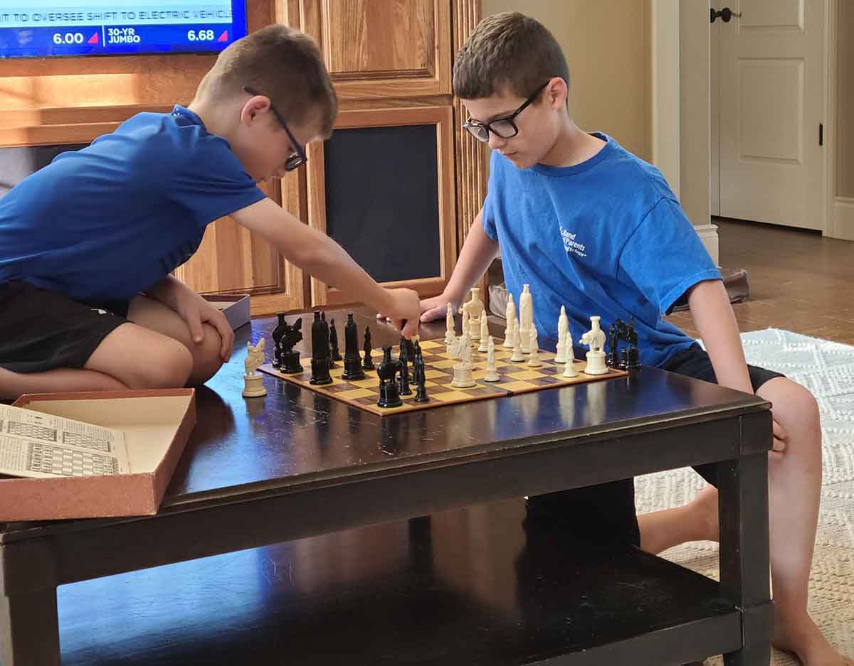 Two boys playing chess on a coffee table.