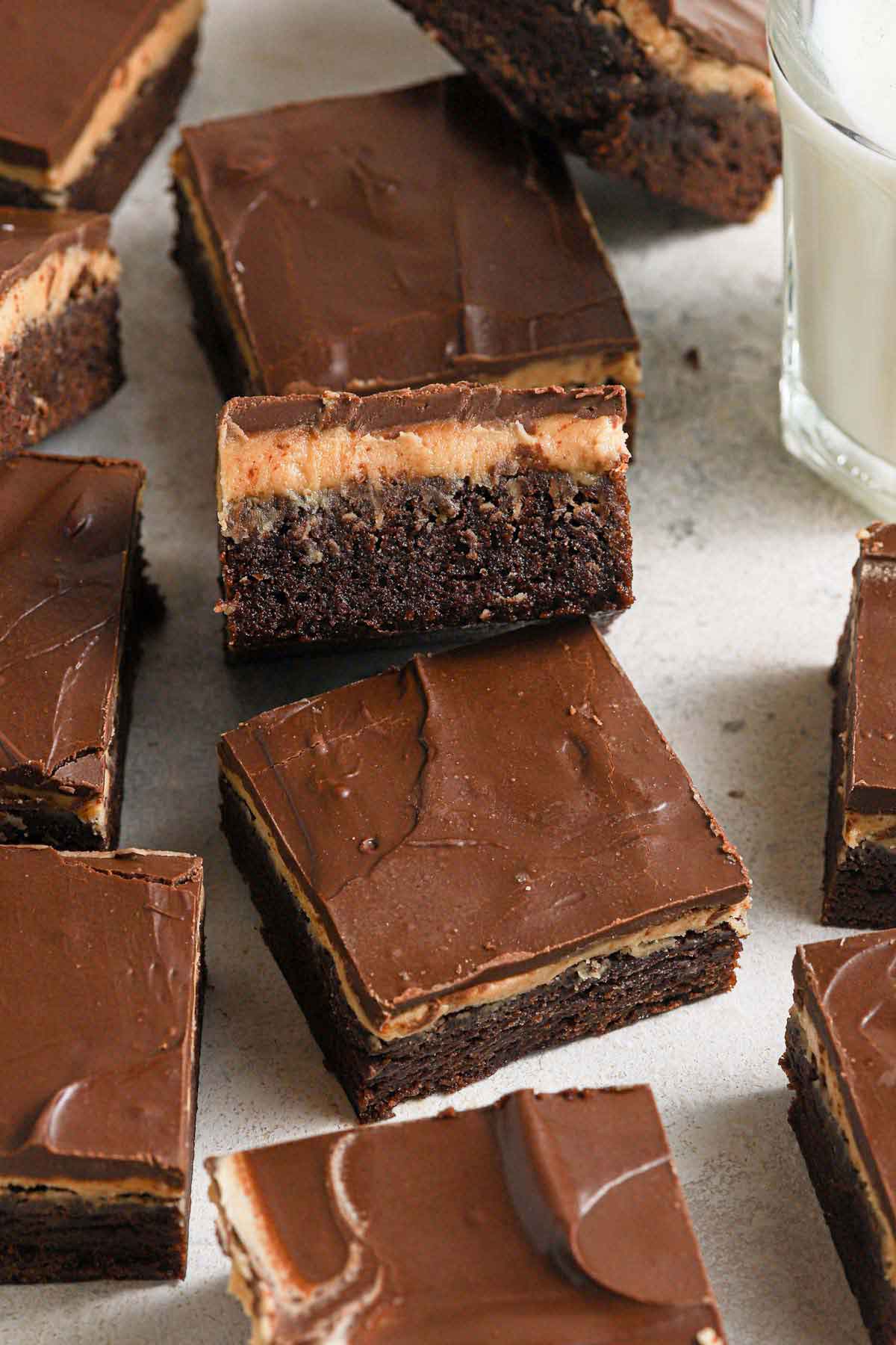 Squares of buckeye brownies sitting on a counter with a glass of milk on the side.