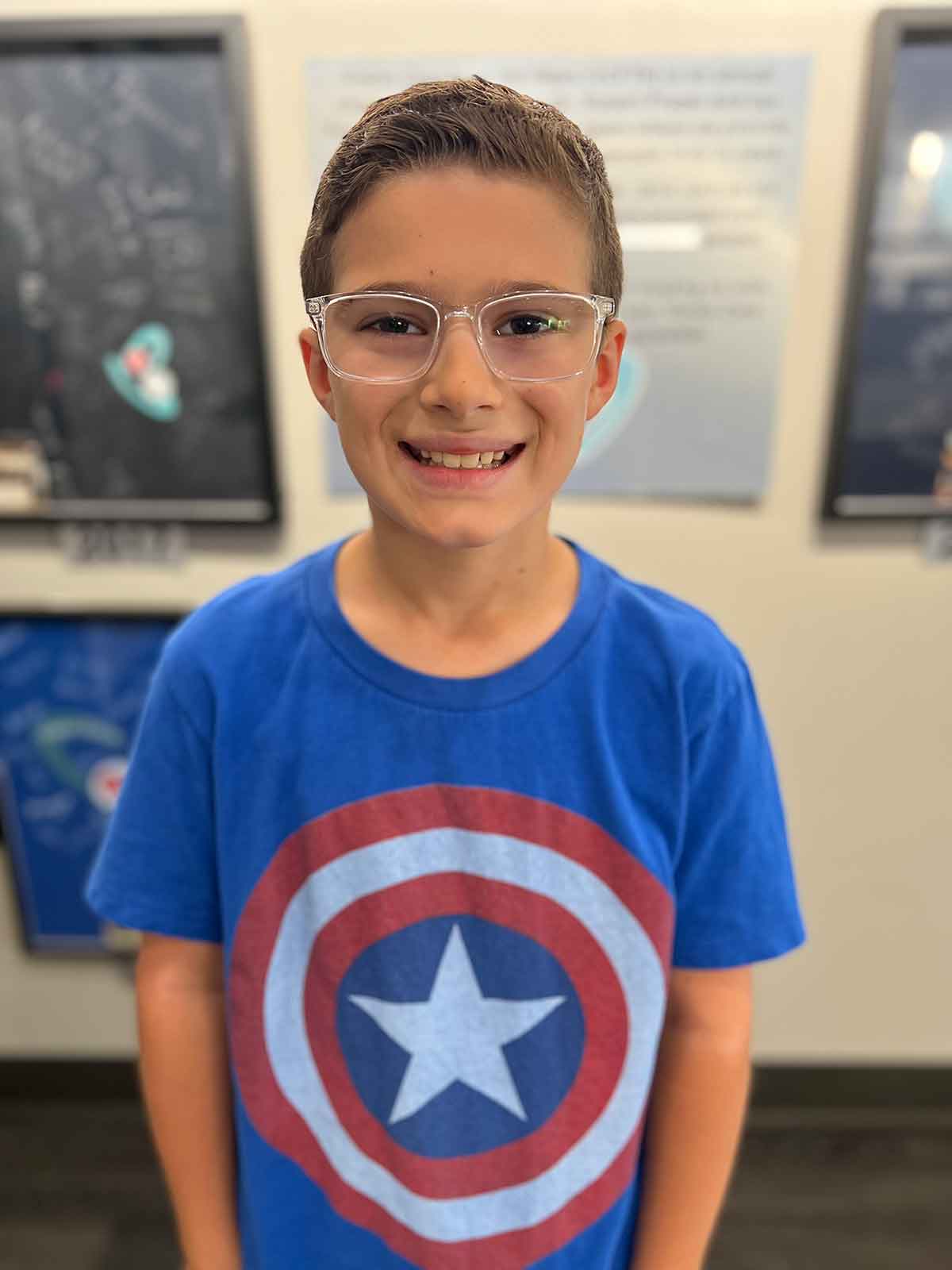 Picture of a boy in a Captain America tshirt wearing glasses with clear frames.
