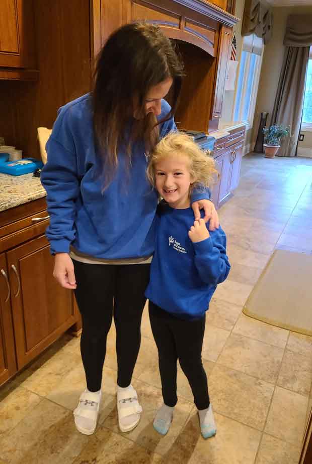 Mom and daughter with arms around each other, each wearing black leggings and blue sweatshirts.