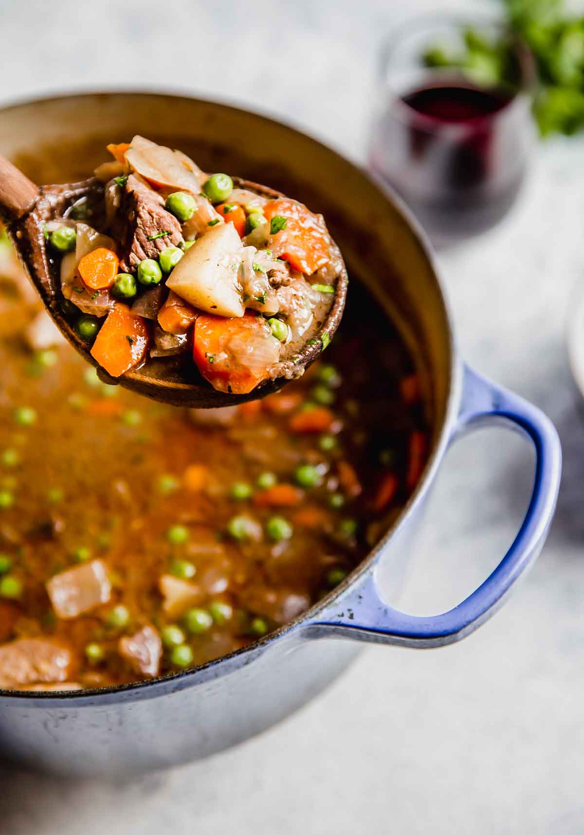A large wooden spoon with a ladleful of beef stew suspended above the pot of beef stew.