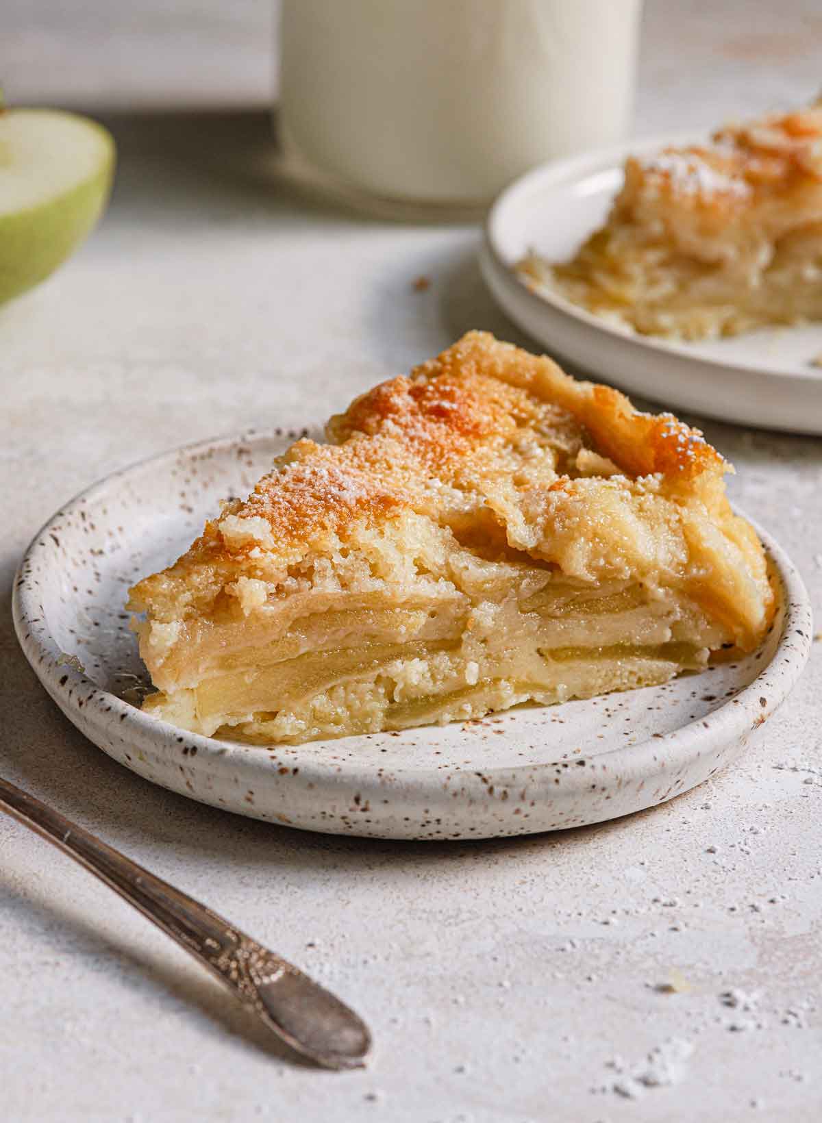 A slice of French apple cake on a white speckled plate.
