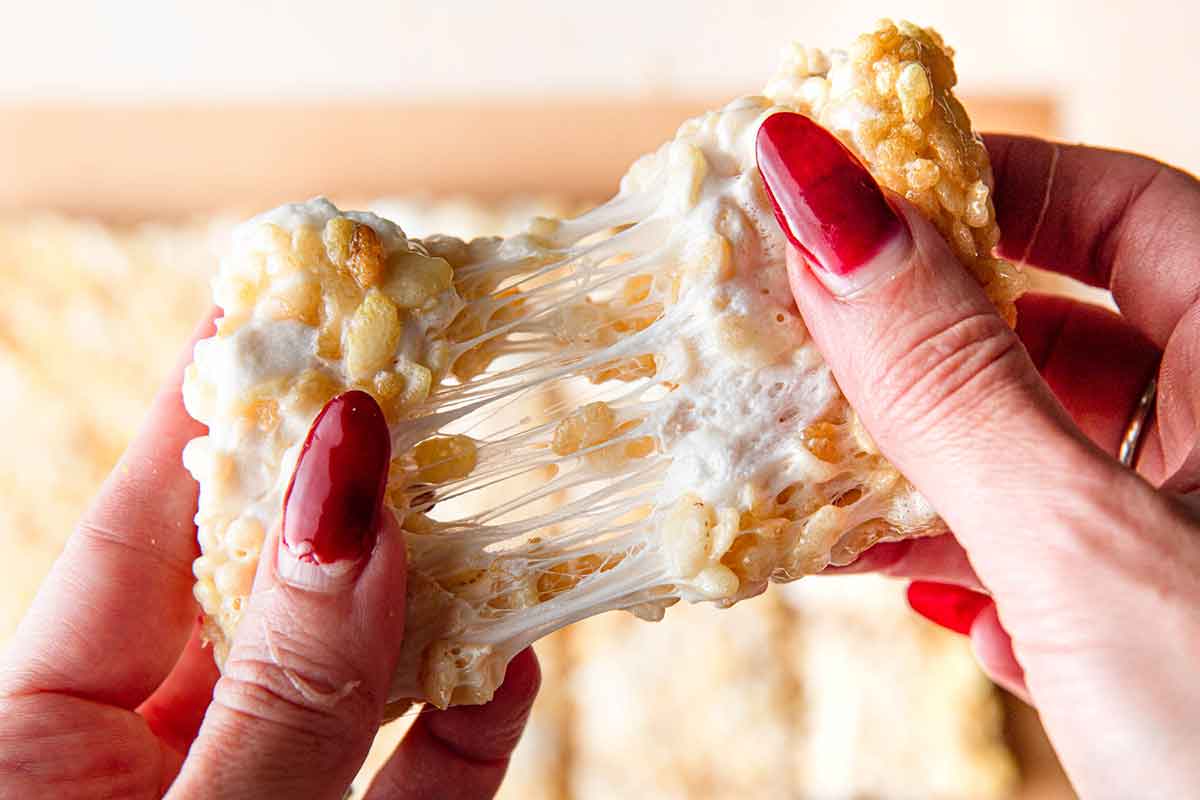 A rice krispie treat being pulled apart, strings of melted marshmallow visible in the middle.