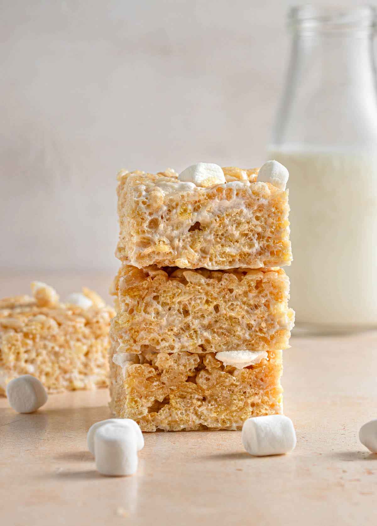 Three rice krispie treats stacked on top of each other with a jar of milk in the background.