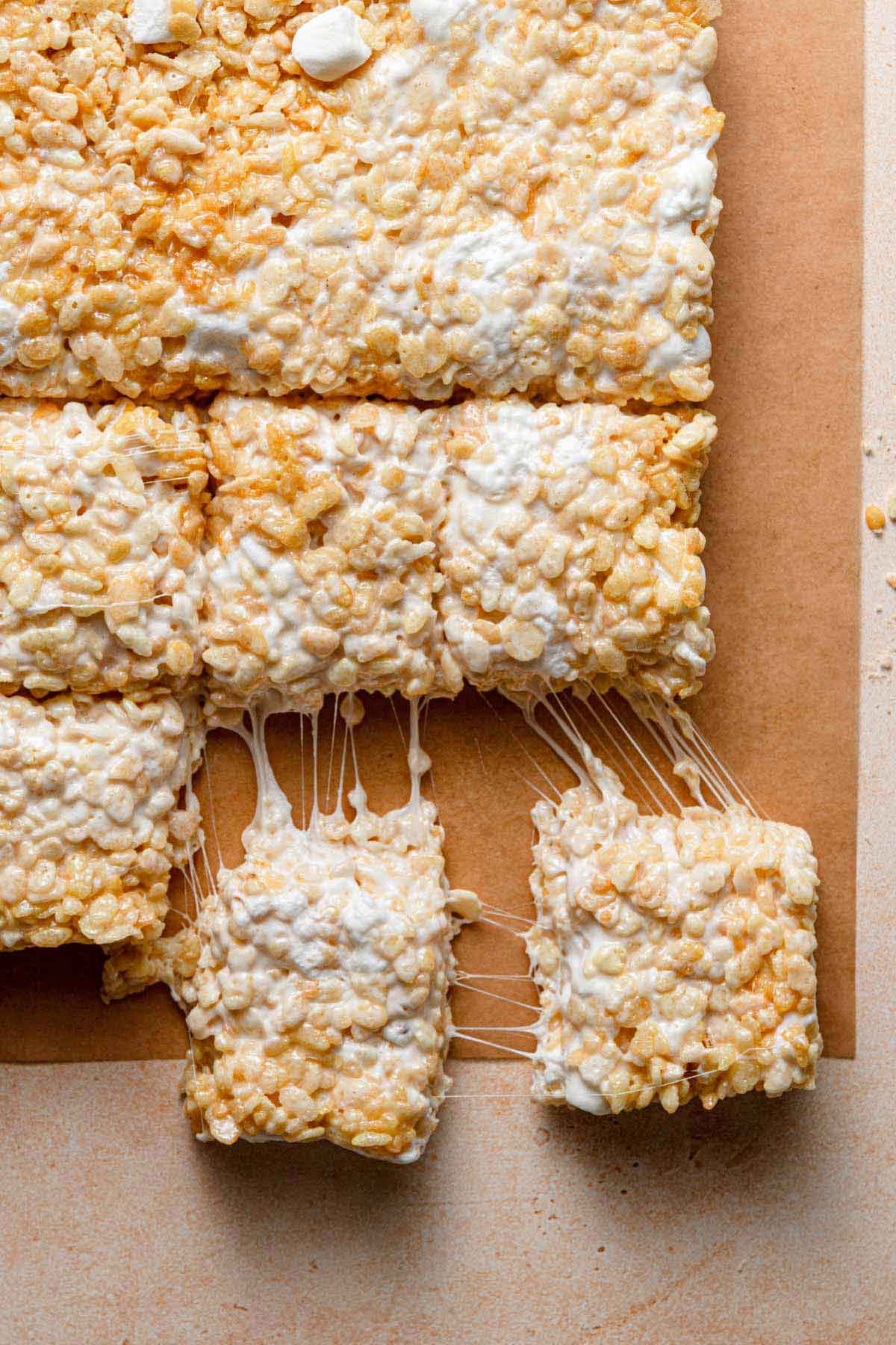 Overhead photo of homemade rice krispie treats on a cutting board, with two being pulled away.