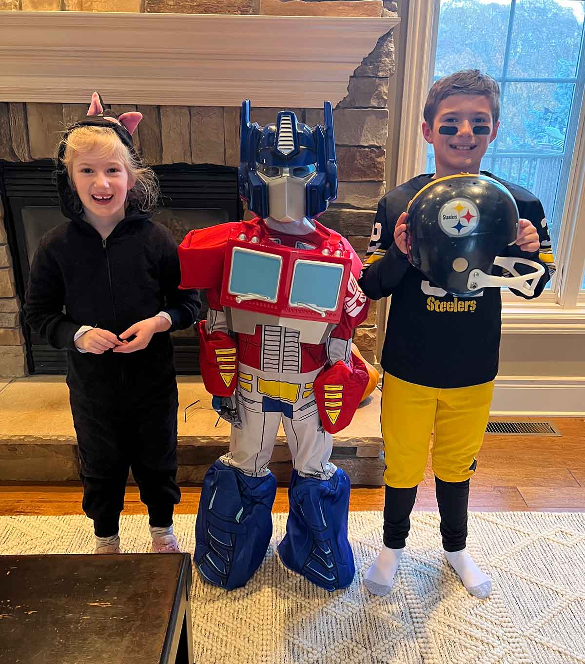Three kids dressed up for Halloween as a black cat, Optimus Prime, and a football player.