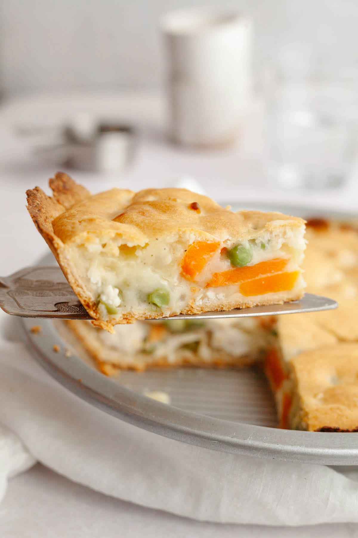 A slice of chicken pot pie on a serving spatula, held above the entire pie.