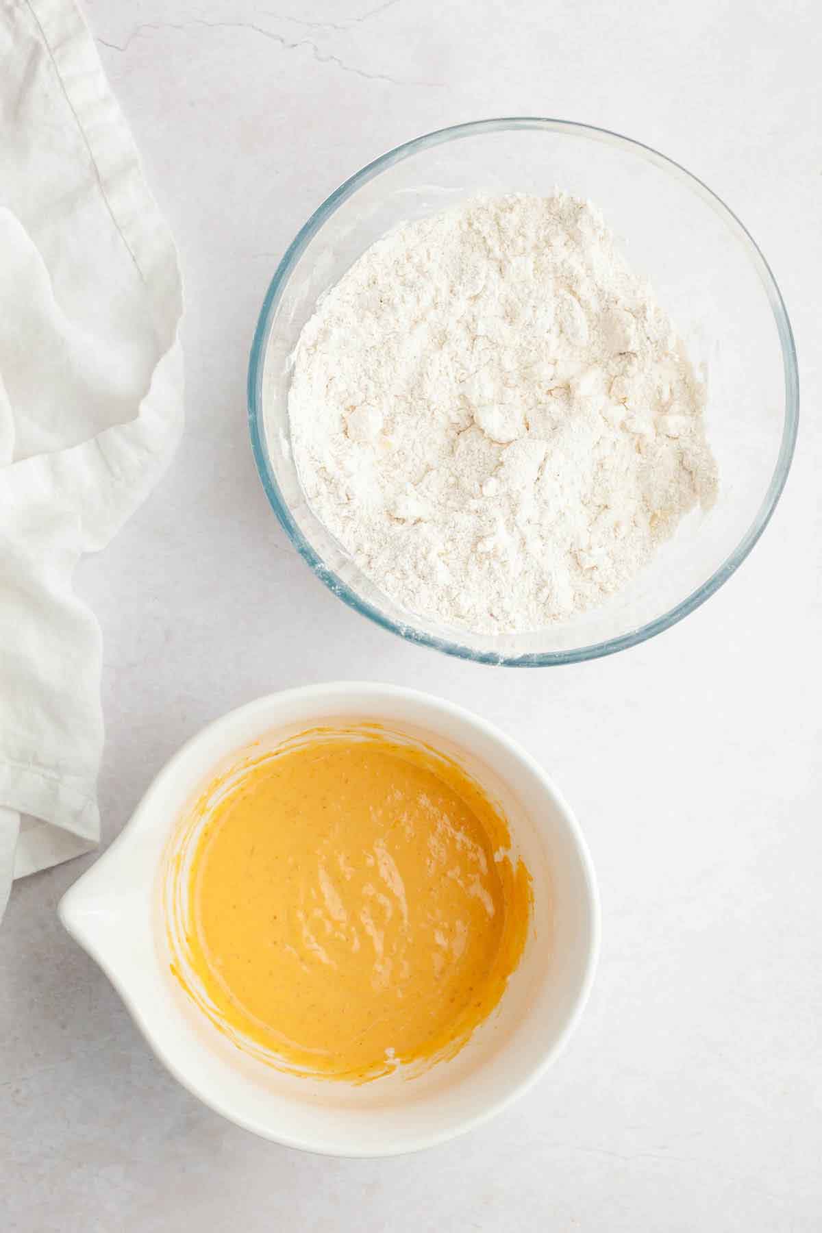 Two bowls, one with dry ingredients and cubed butter, the other with wet ingredients for pumpkin scones.