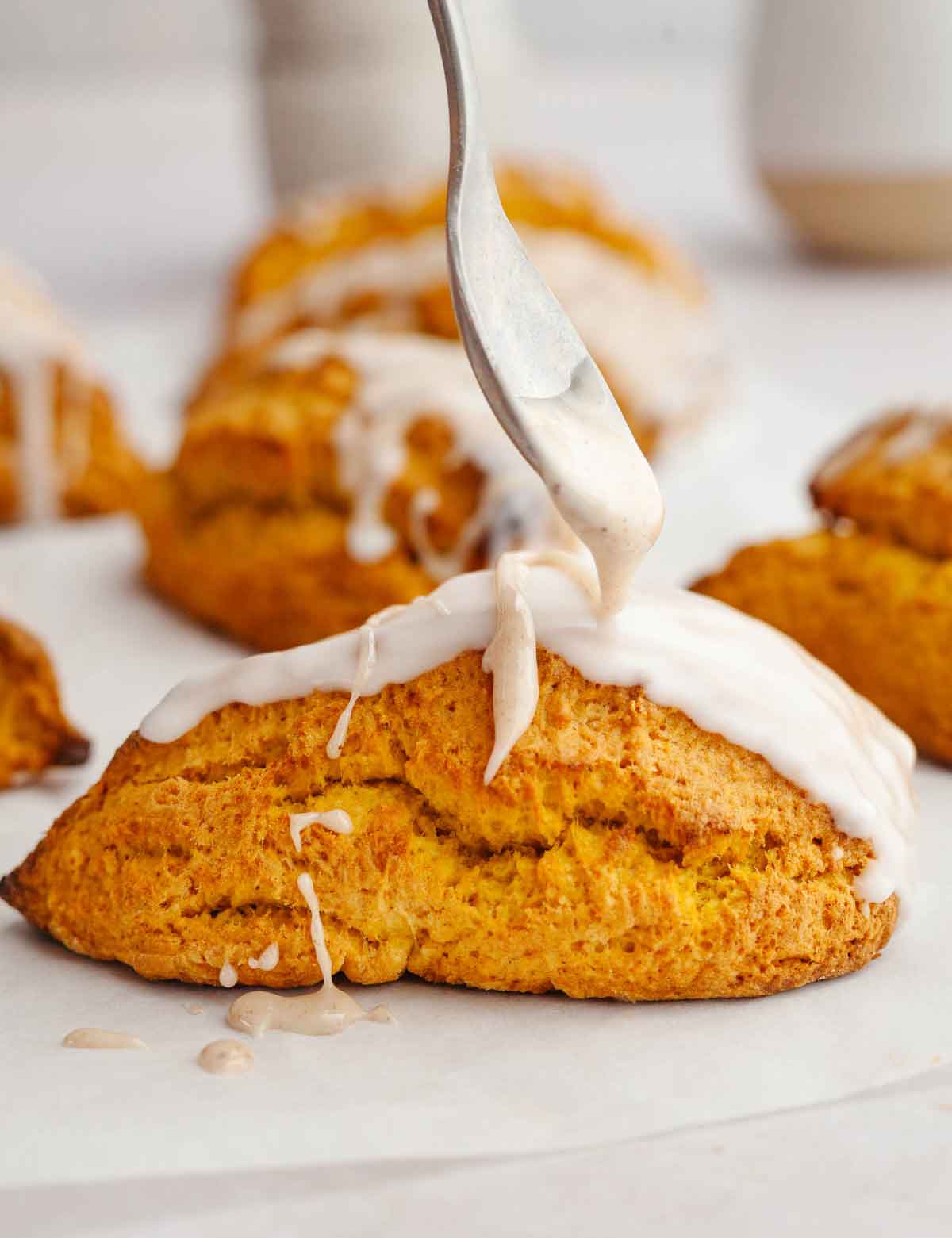 A spoon drizzling spiced glaze onto a pumpkin scone.