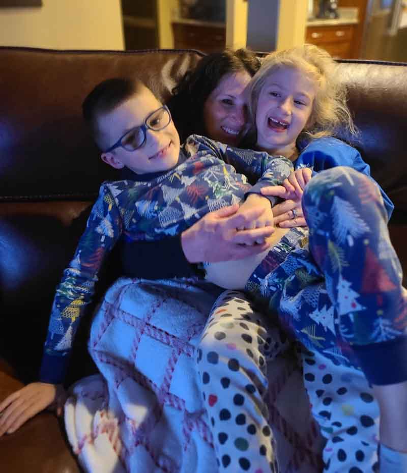 Mom with a little girl and little boy sitting on top of her on a couch.