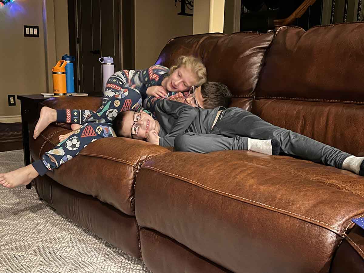 Two boys and a girl in pajamas piled on top of each other on a couch.