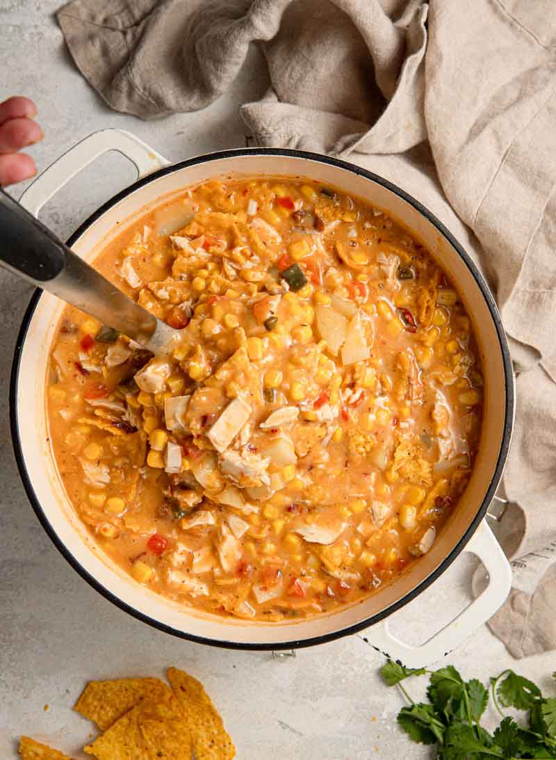 Overhead photo of a chicken and corn chowder being ladled out of a large Dutch oven pot.