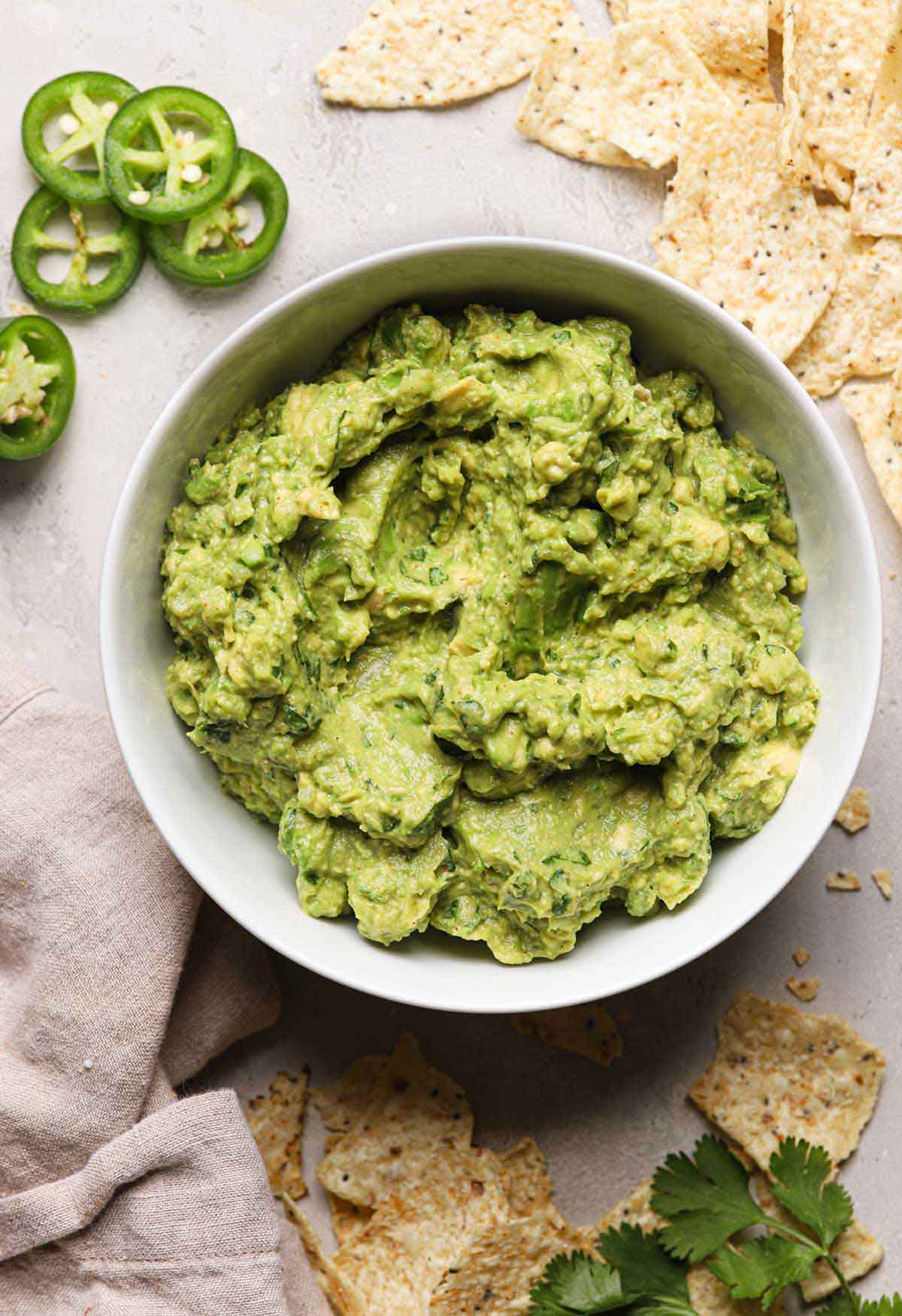 Overhead photo of a bowl of guacamole surrounded by tortilla chips and slices of jalapeno.