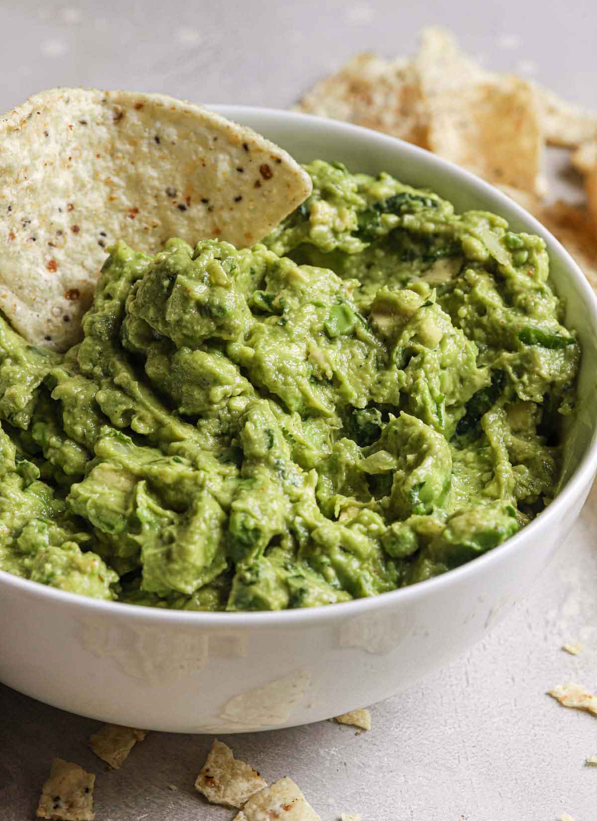 Close up photo of a bowl of guacamole with a tortilla chip dipped into it.