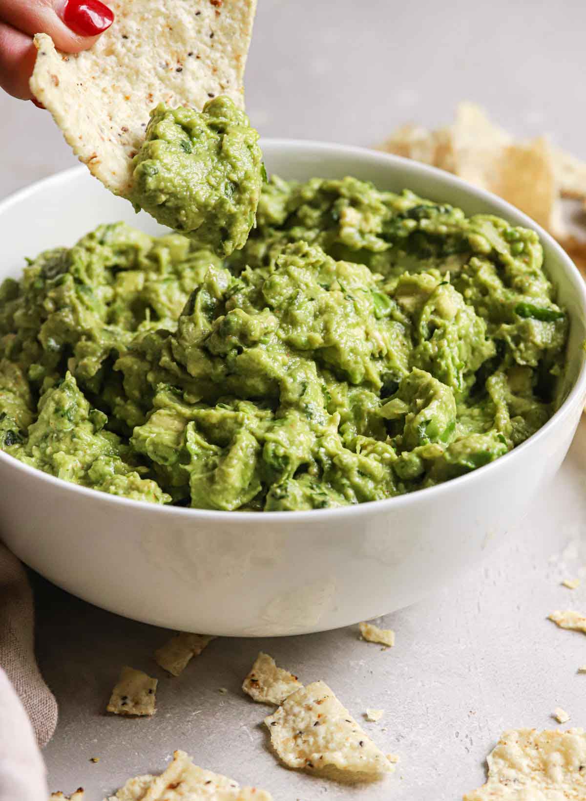 A tortilla chip being dipped and lifted out of a bowl of guacamole.
