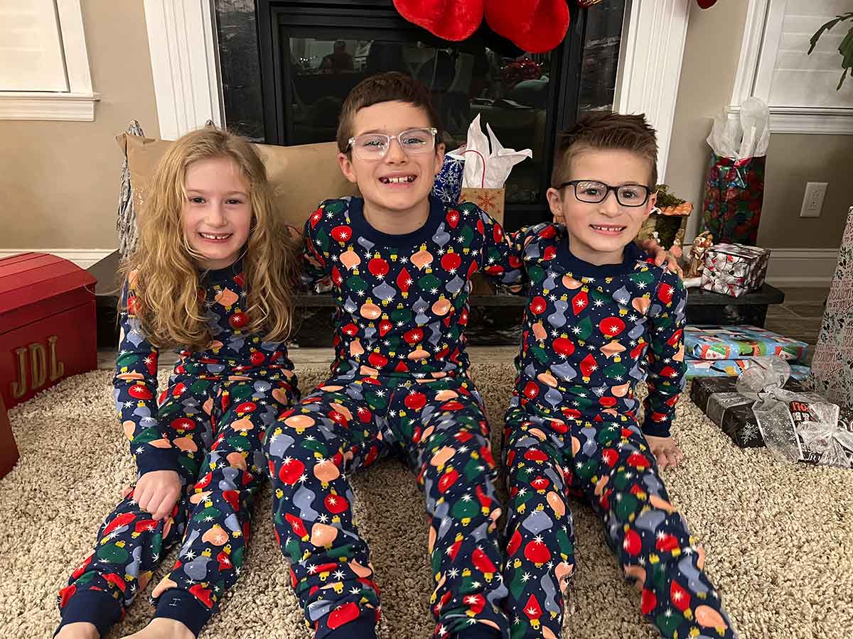 A girl and two boys sitting next to each other on the floor in Christmas pajamas.