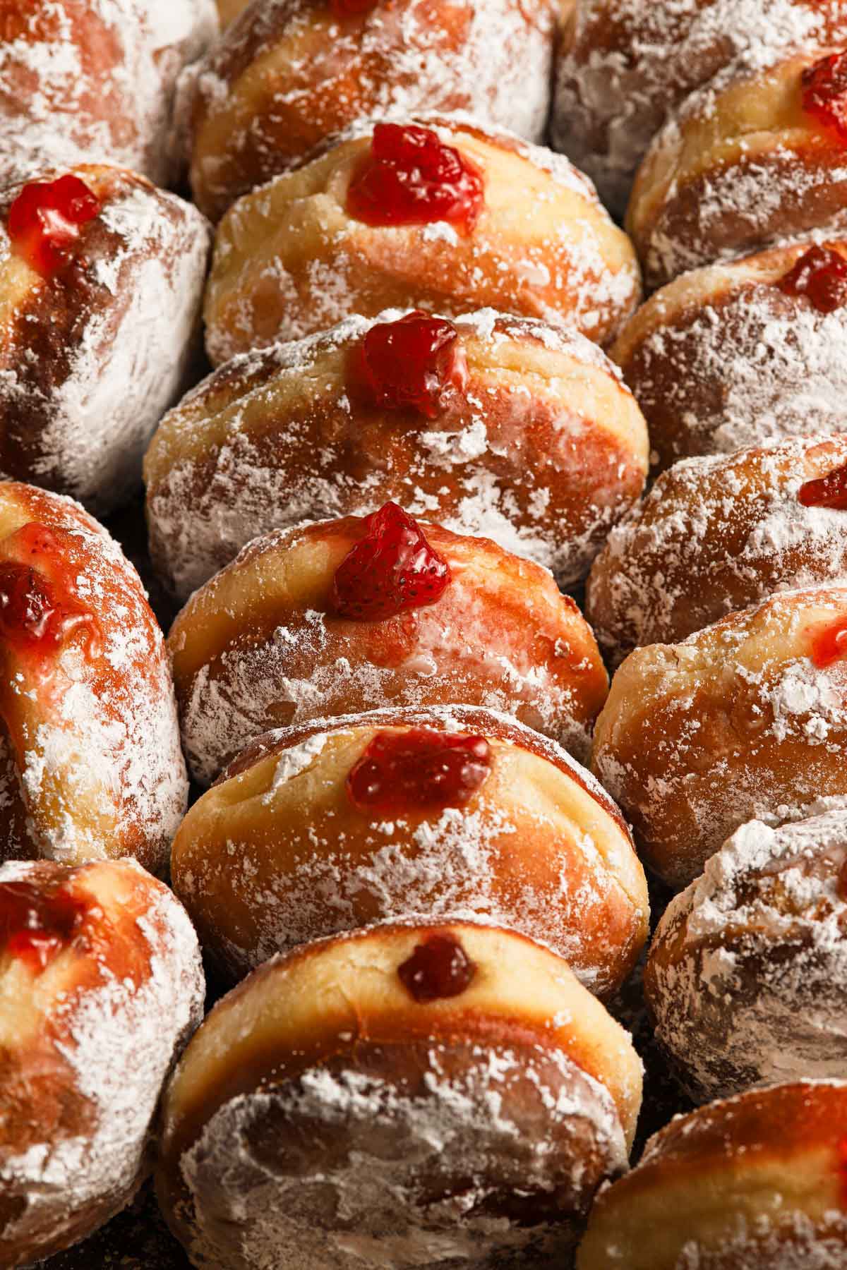 Close up photo of paczki lined up close together with the fruit preserves peeking out of the filled doughnuts.