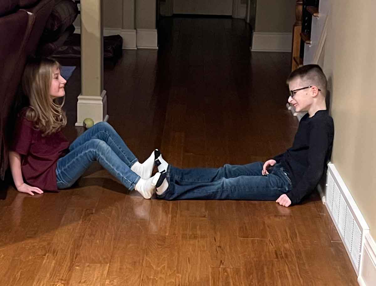 Boy and girl sitting across from each other on the floor with their feet out and touching.