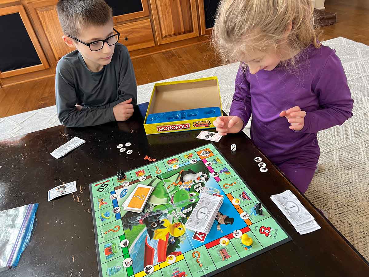 A boy and girl sitting around a coffee table playing a game of Monopoly.