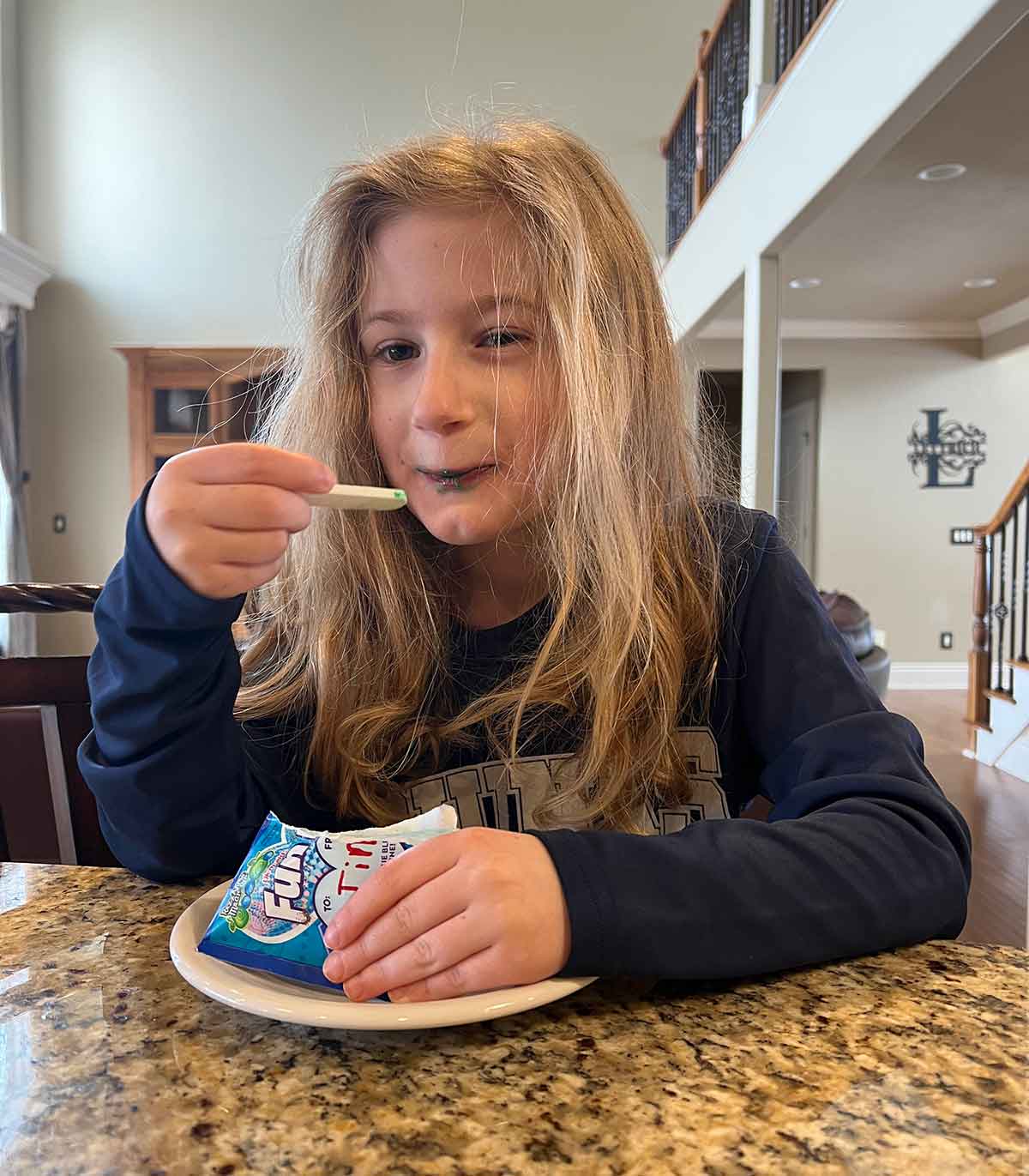 Little girl with blonde hair sitting at a counter eating Fun Dip candy.