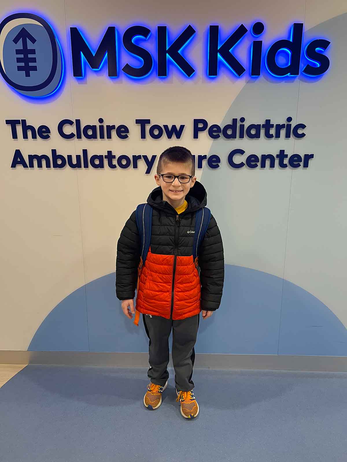 Little boy standing in a hospital lobby in front of a sign that says MSK Kids.
